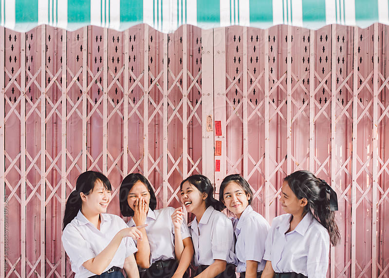 Asian high school girls standing in front of pastel pink garage door in Thailand