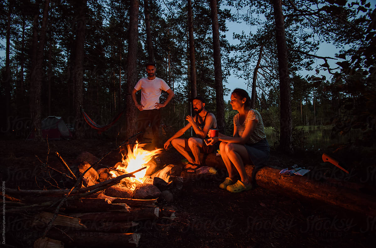 Friends near bonfire in camping zone in the forest.