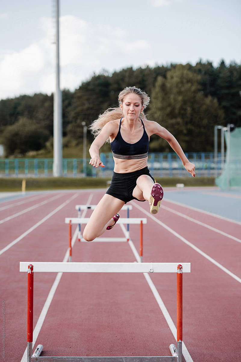 Female athlete leaping over barrier at stadium