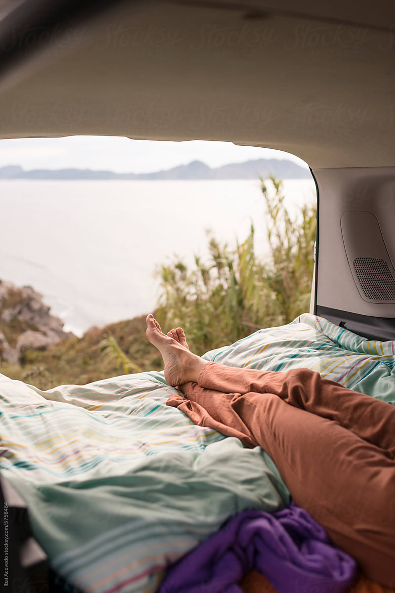 Woman resting on camper van bed with beautiful view