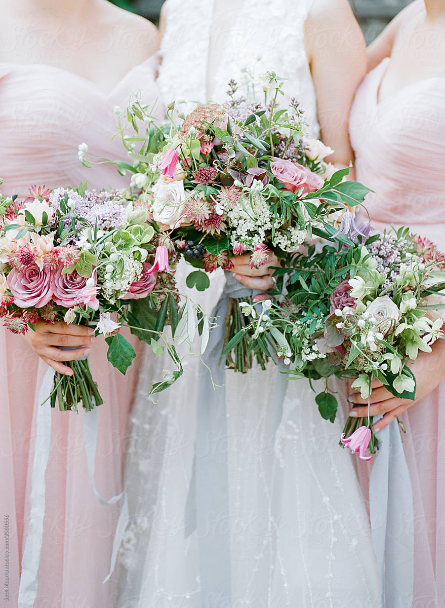 A bride & her bridesmaids hold delicate green & pink floral bouquets with silk ribbon
