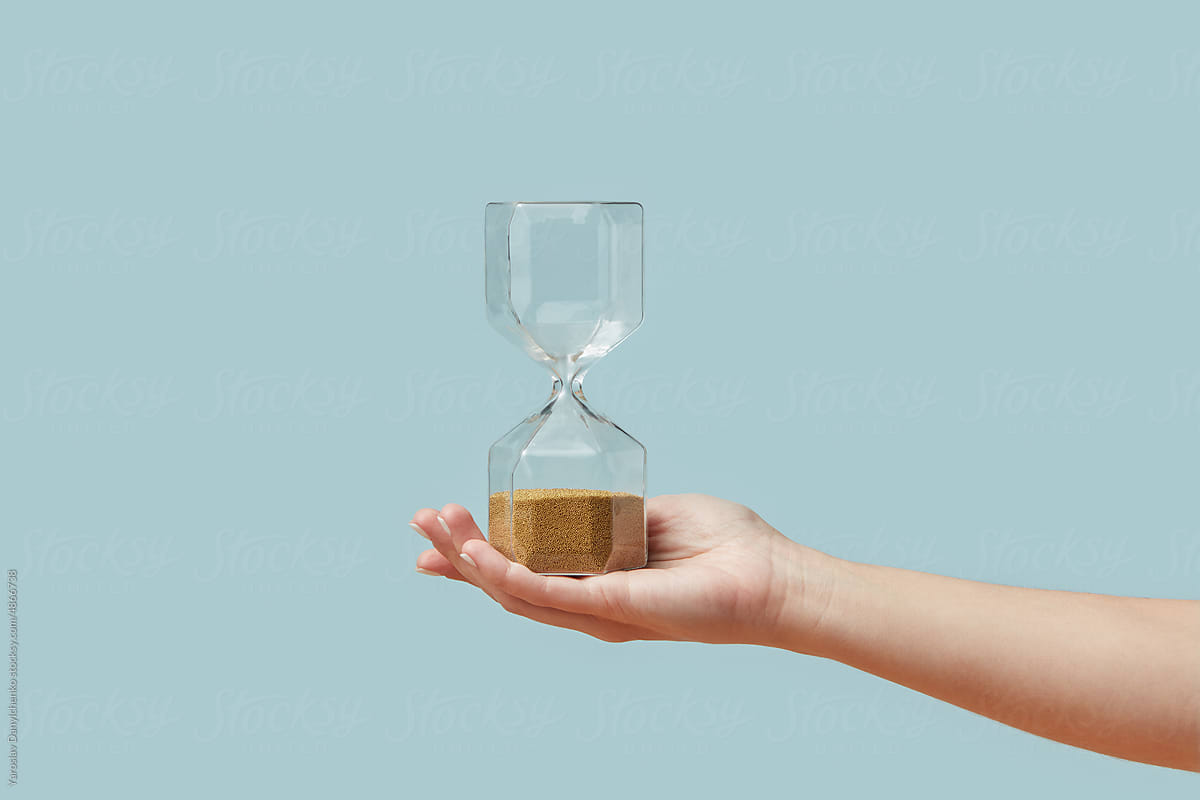 Hourglass with golden sand in woman\'s hand.