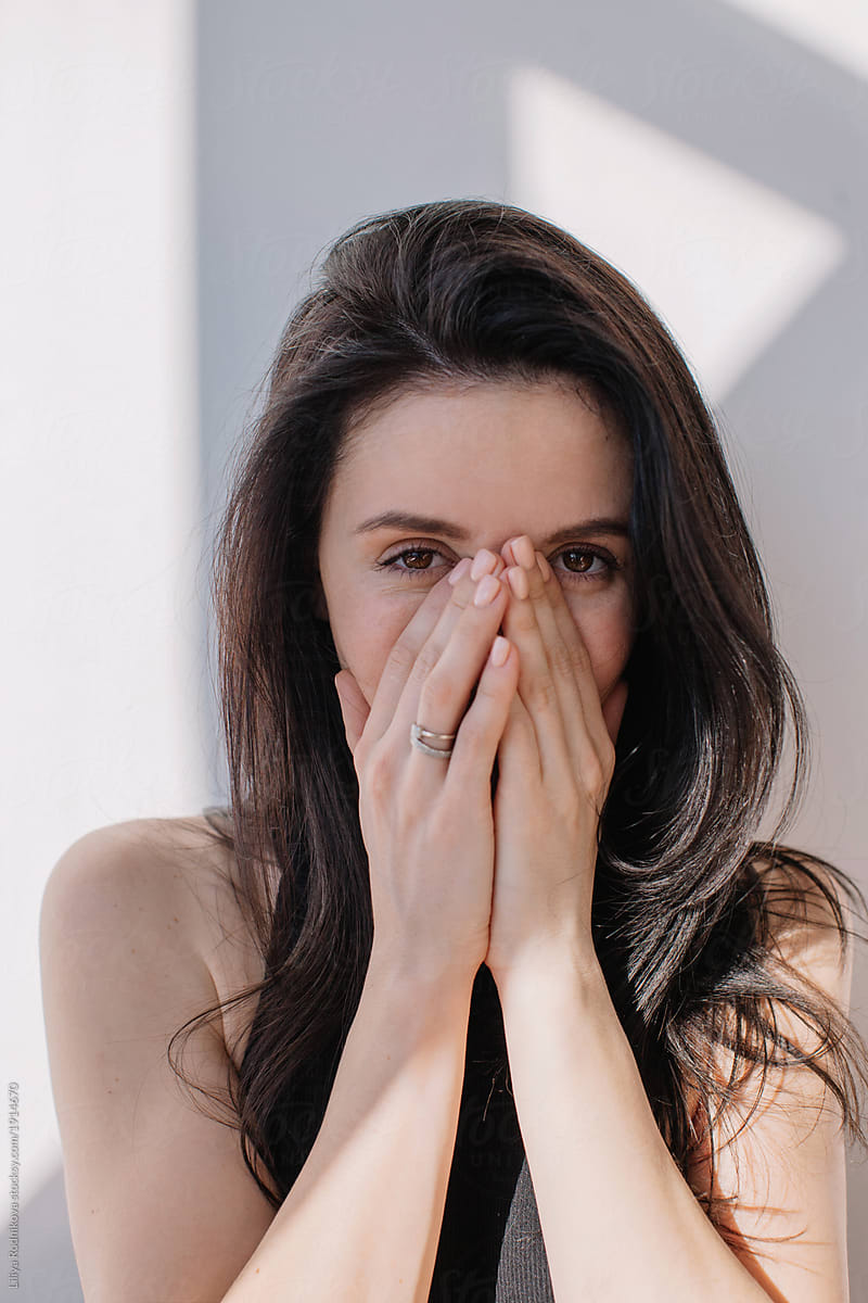 Pretty brunette woman hiding half of her face with hands and looking at camera
