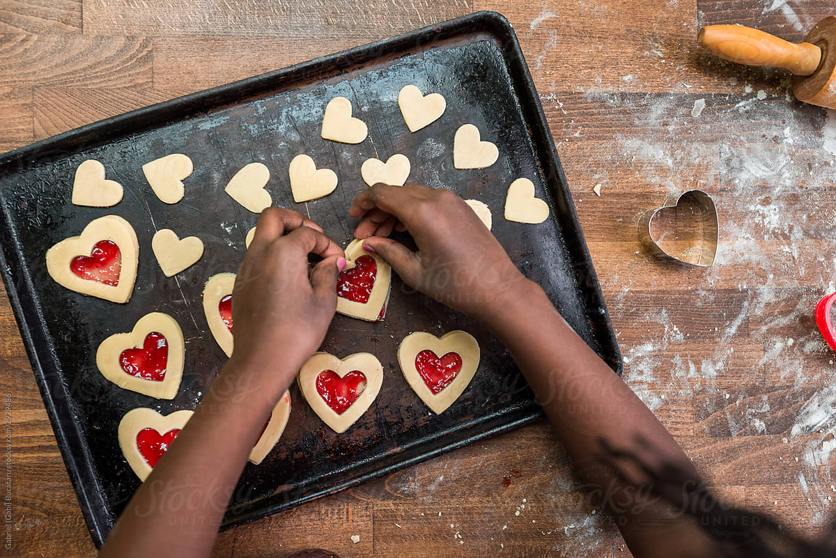 Black girl\'s hands placing a heart shaped cookie in a baking tra