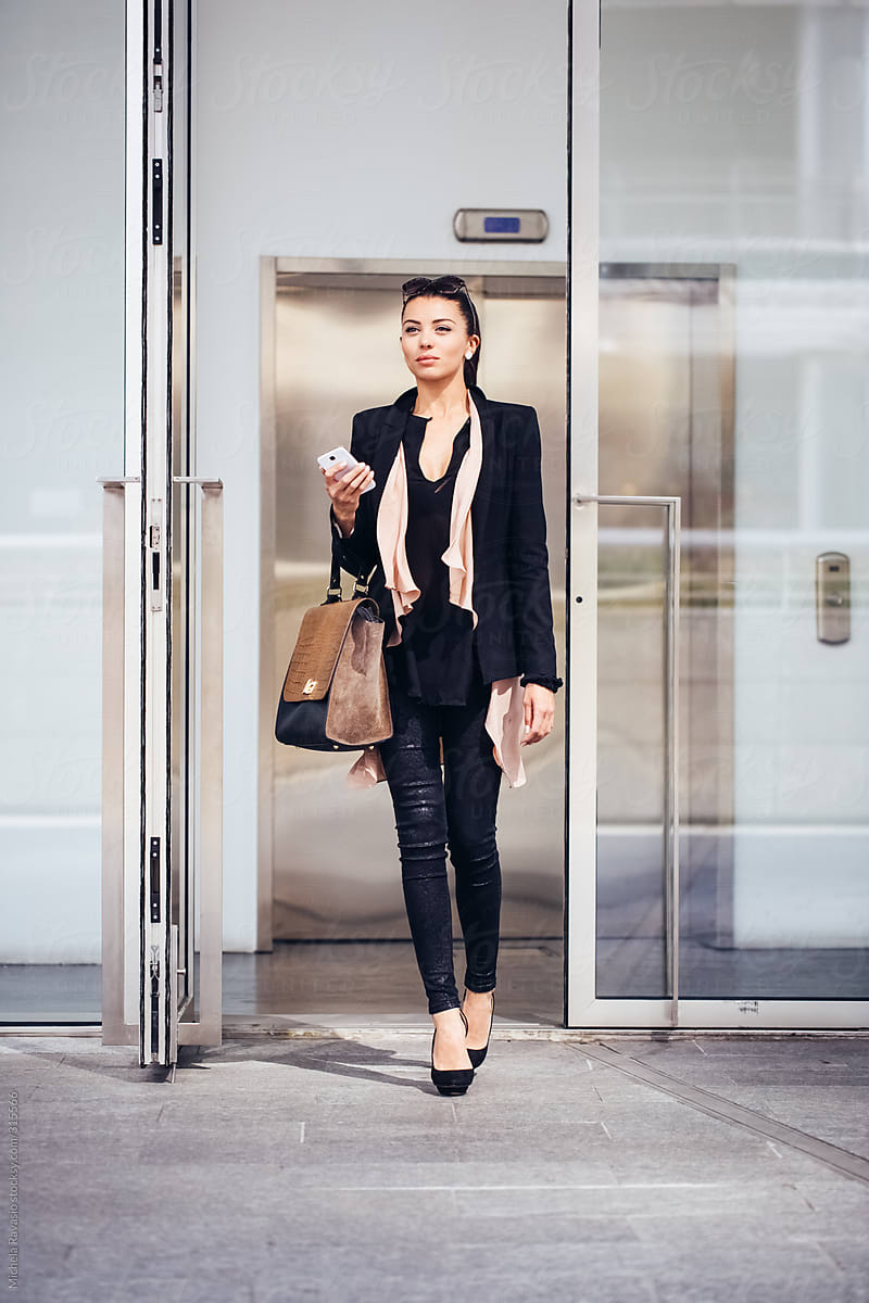 Attractive business woman walking out of a office building holding a smart phone