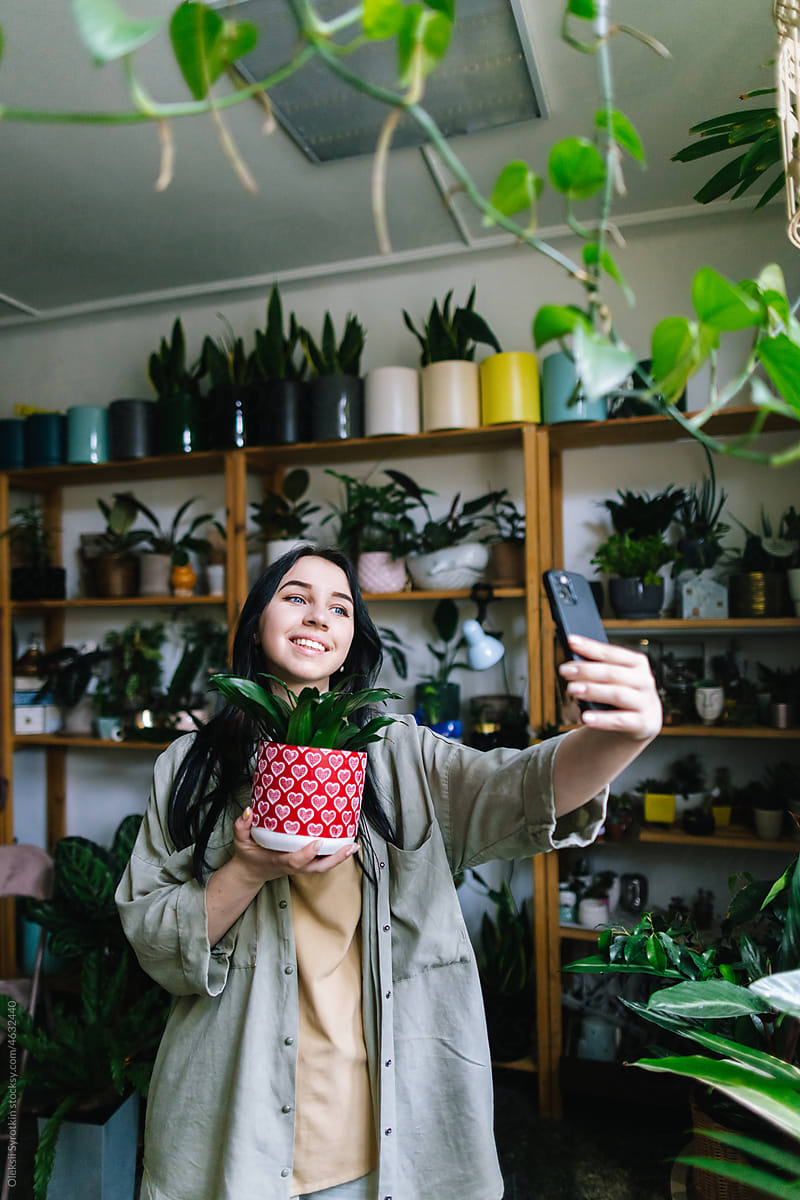 Cheerful girl taking selfie with houseplant in modern studio