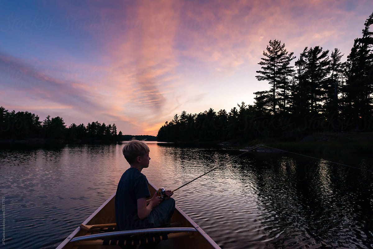 Boy fishing from canoe on serene lake at dusk in Muskoka