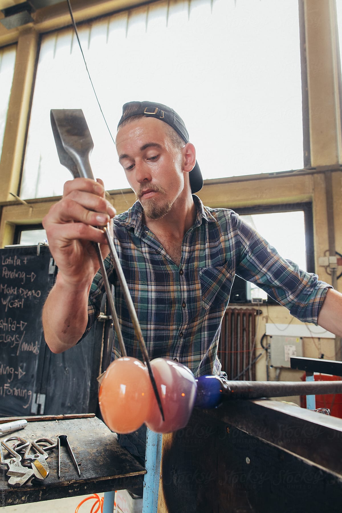 Artisan Glass Workshop - Portrait of Male Hipster Artist Shaping Hot Orange Glass With Jacks