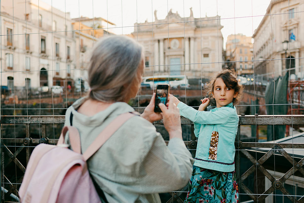 Grey-haired woman taking a photo of granddaughter on her cell phone