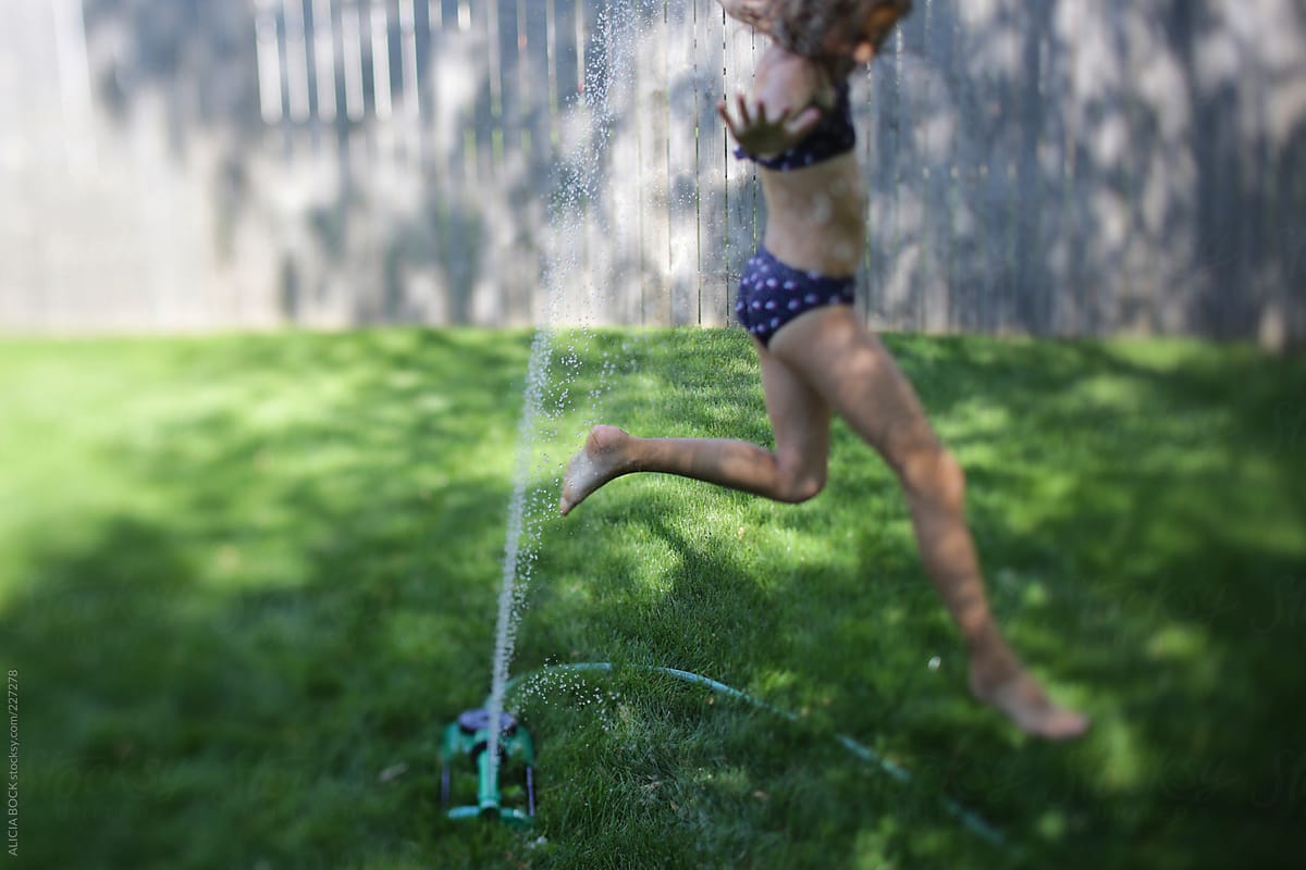 Girl Running Through A Sprinkler On A Hot Summer Afternoon