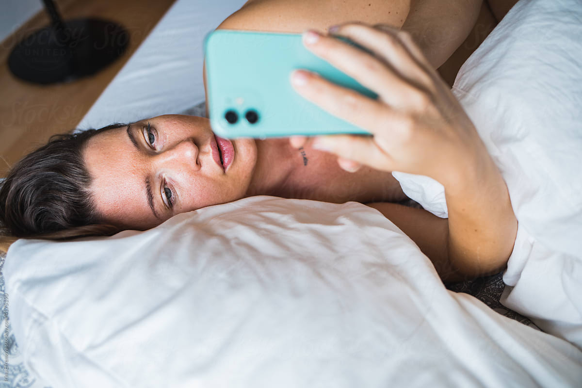 Woman in bed on the phone texting smiling