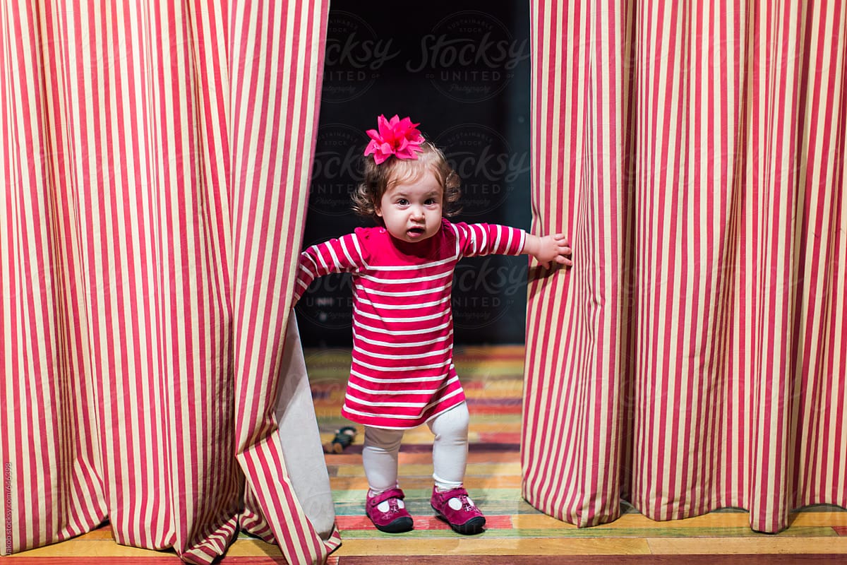 Cute toddler in striped dress walking on a theatre stage with matching curtains