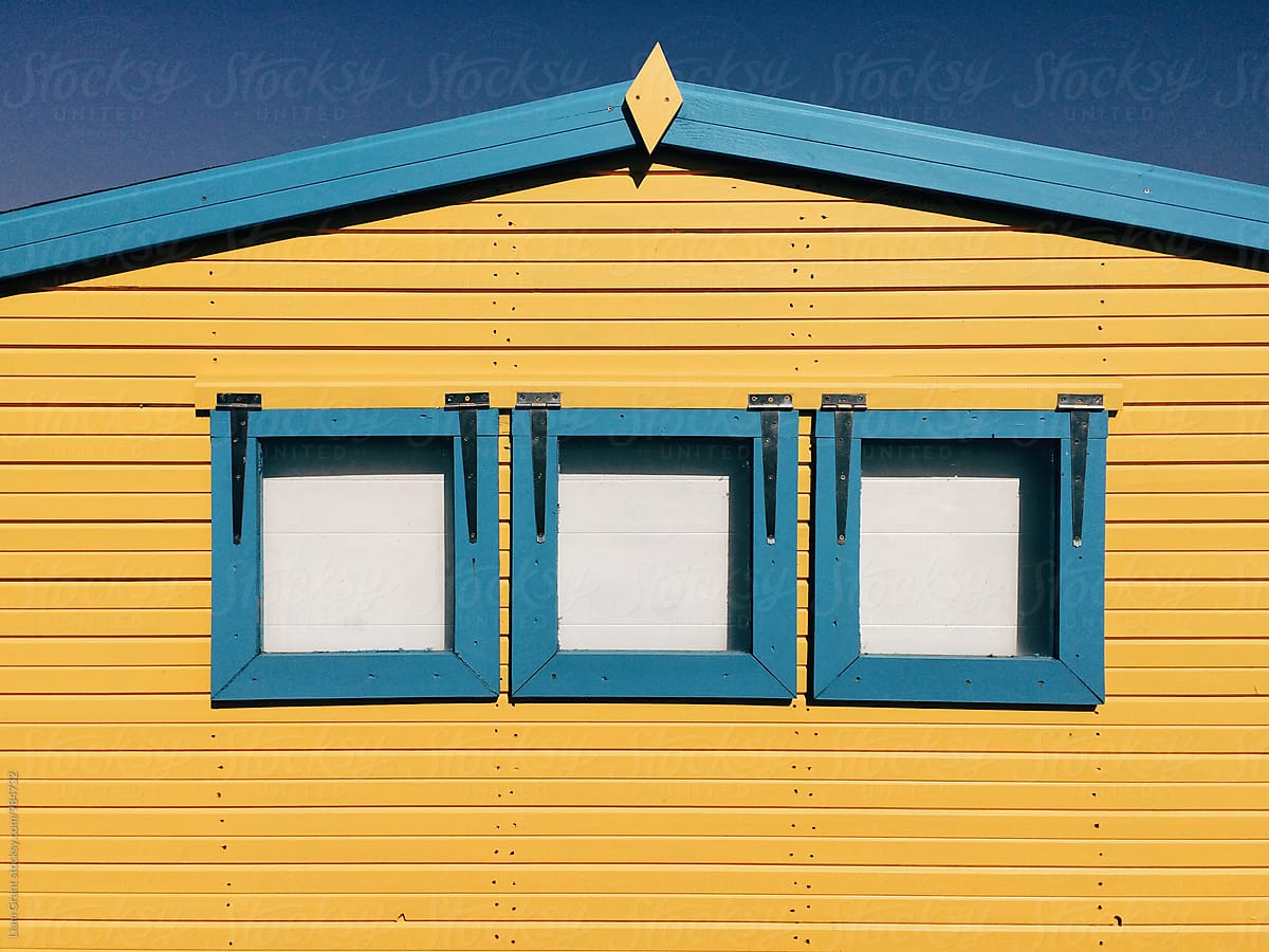 Yellow wooden panelled beach hut with blue windows. Norfolk, UK.