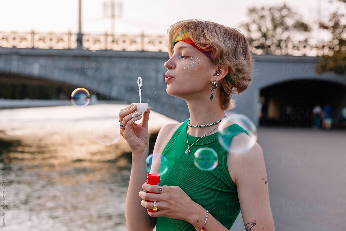 Young queer woman blowing bubbles on street