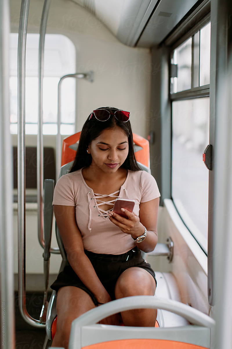 Young Indian woman typing message on mobile phone while travelling on the bus