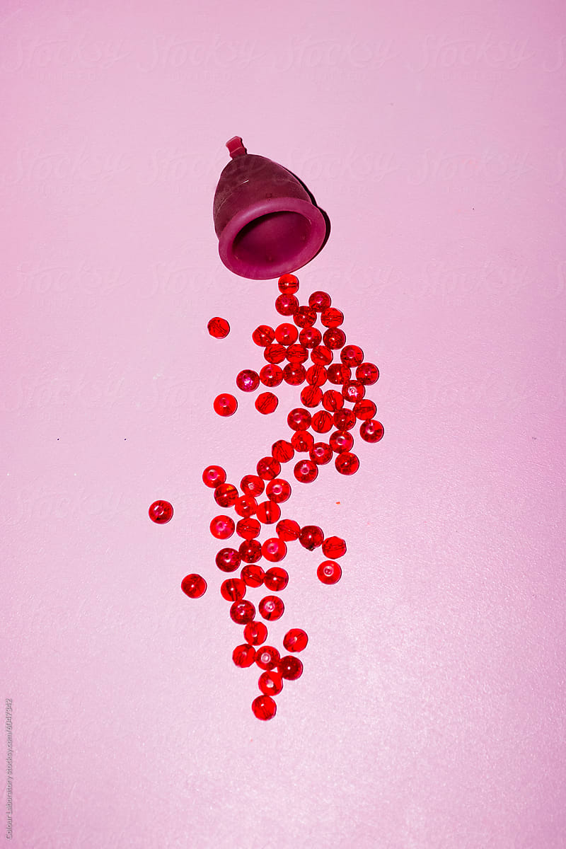 Conceptual period photo of period cup and red pearls as blood