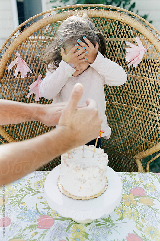 girl covers eyes while dad lights birthday cake