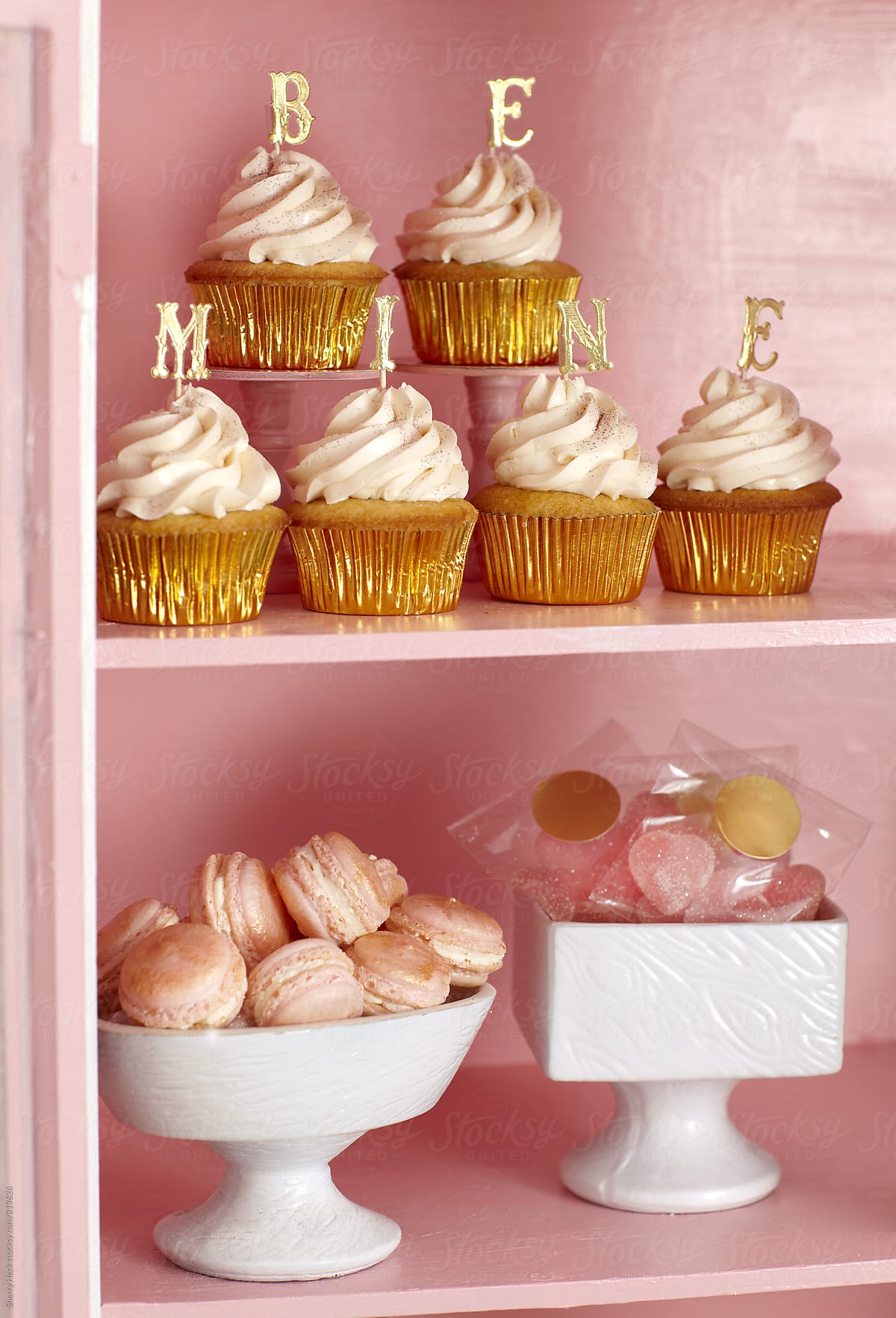 Be Mine gold letters on cupcakes in pink cabinet with macaroons and candy