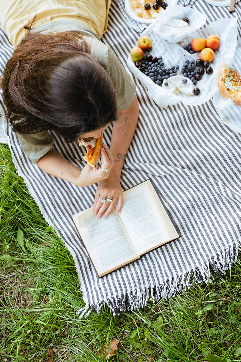 Brunette woman reading book and eating pizza in park