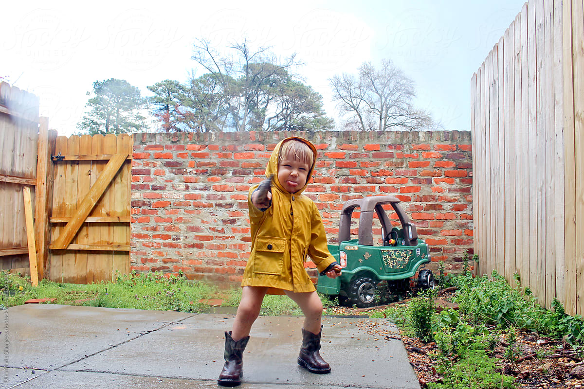 Toddler In Raincoat and Boots Making Silly Face Outside