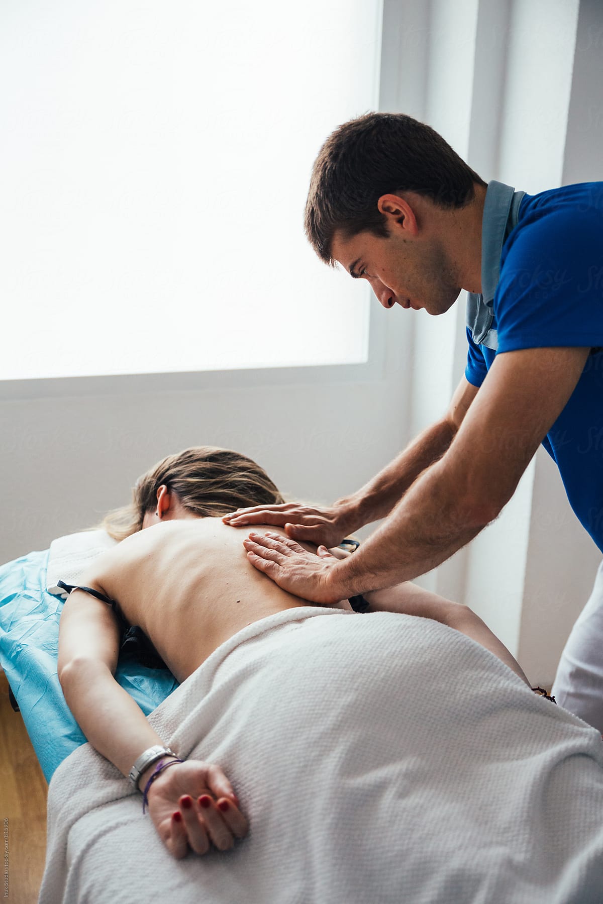 Young woman lying on her front on a bed receiving a massage on her back by a male therapist