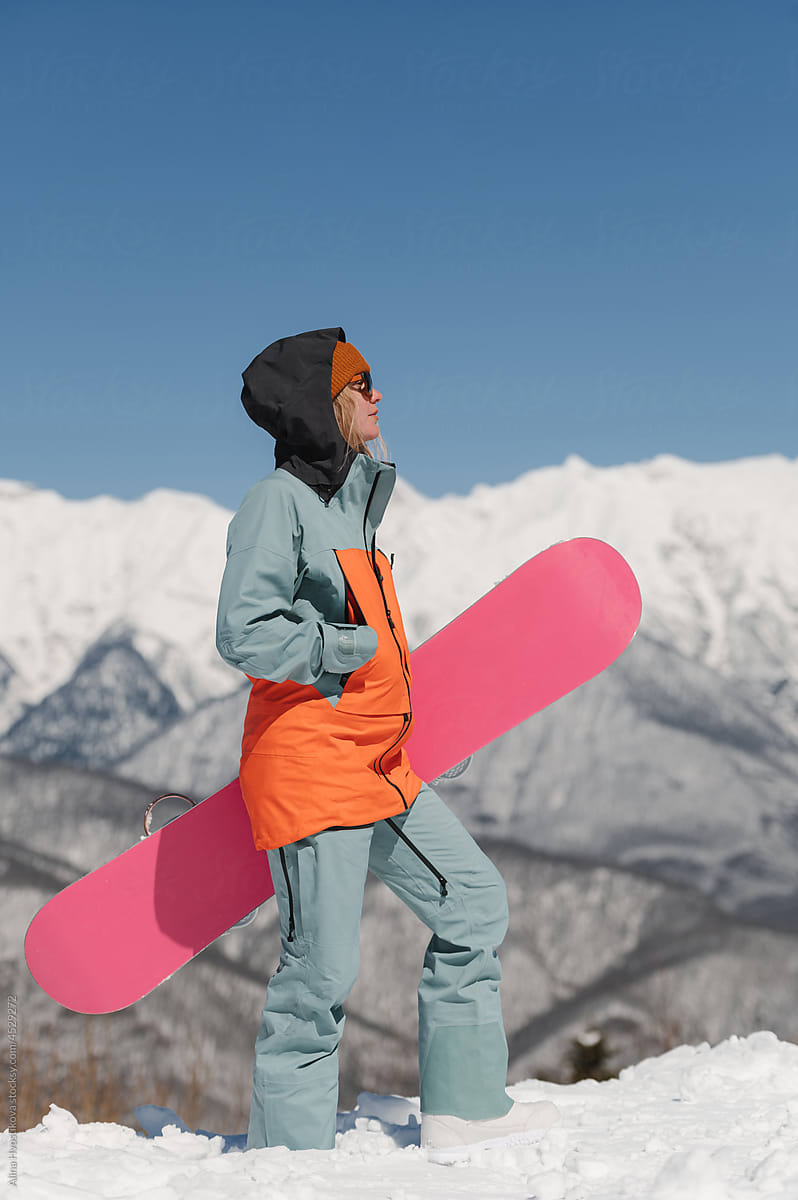 Athletic lady with snowboard standing on snowy terrain