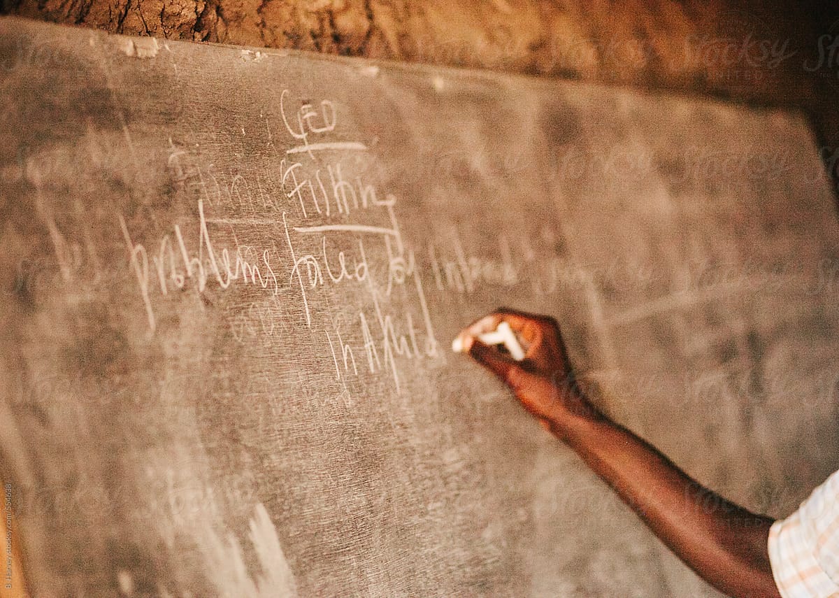 College-Aged Rwandan Boy Writes on a Blackboard