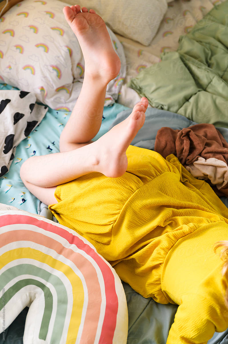 Little Girl Kicking Feet while Lounging on Colorful Bed