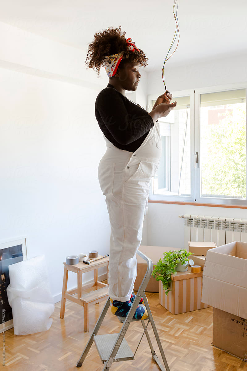 Pregnant woman in ladder fixing electric installation in new home