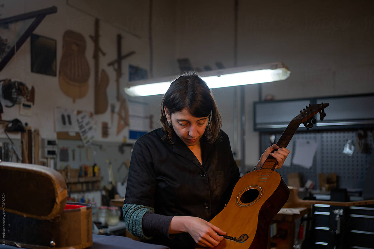 Luthier Woman Checking An Old Guitar In The Workshop.