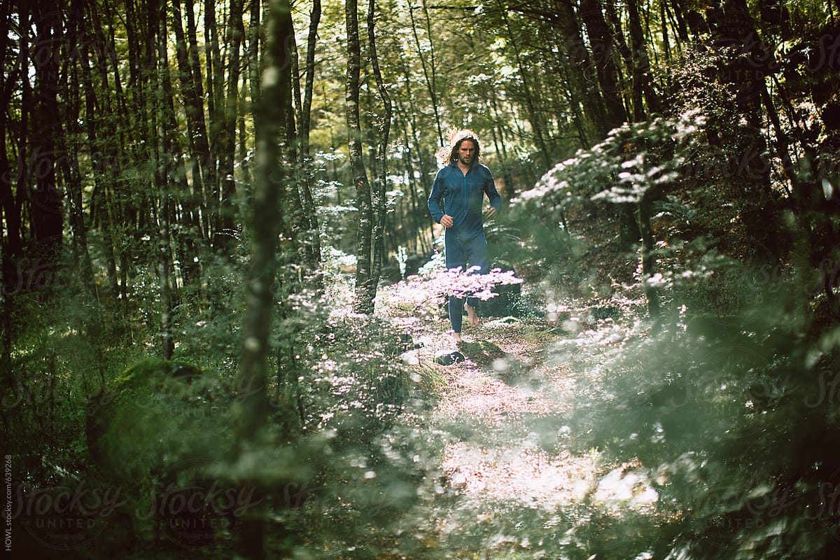 A long haired brunette man runs barefoot through the forest
