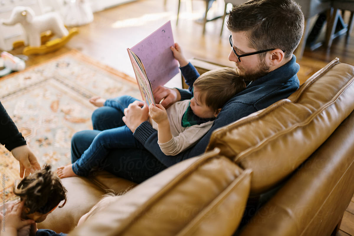 father and son reading story book together on couch in home