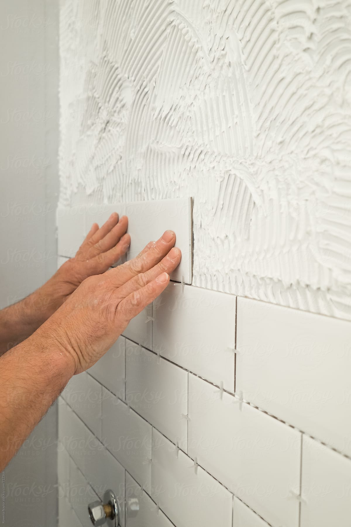 Man laying white tiles in bathroom shower