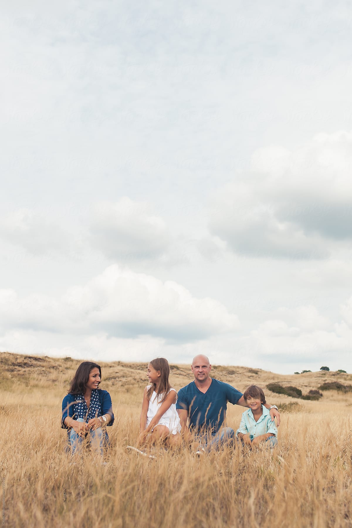 Family of four sitting in a golden field underneath a big cloudy sky