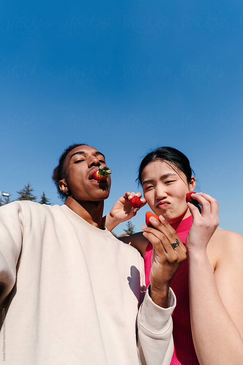 Funny selfie of multiracial couple eating strawberries