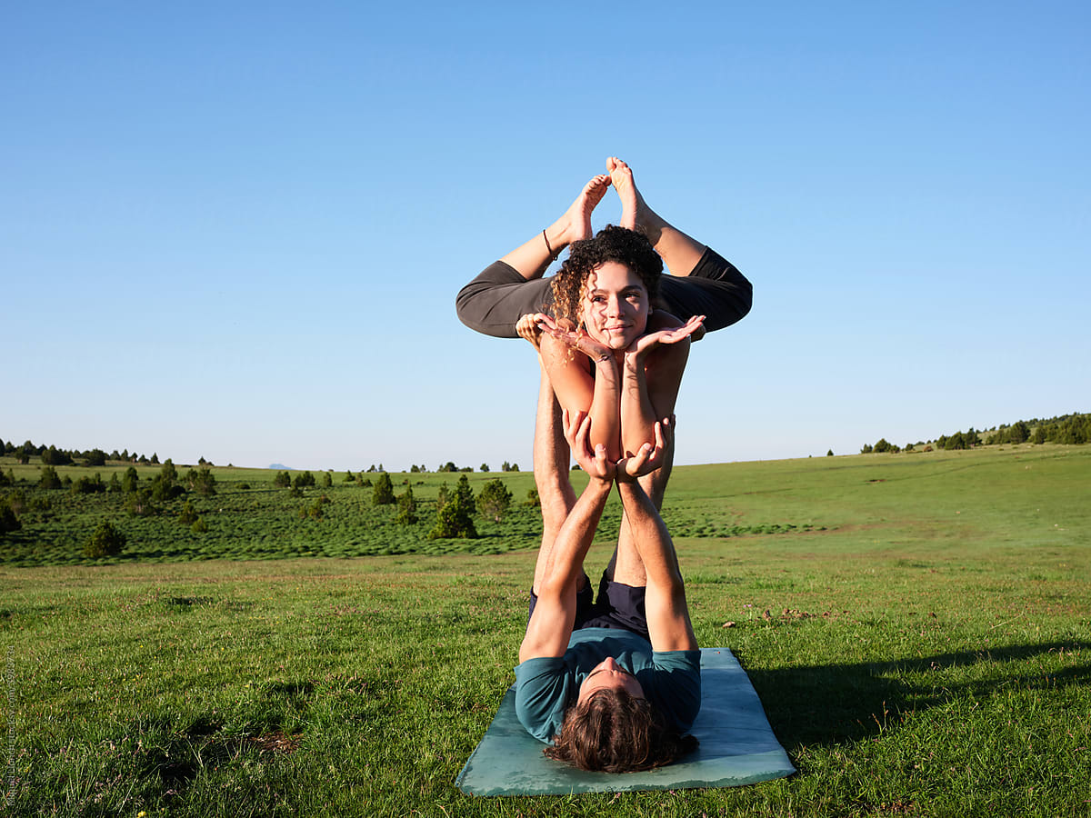 Couple performing acro yoga pose on sunny green meadow
