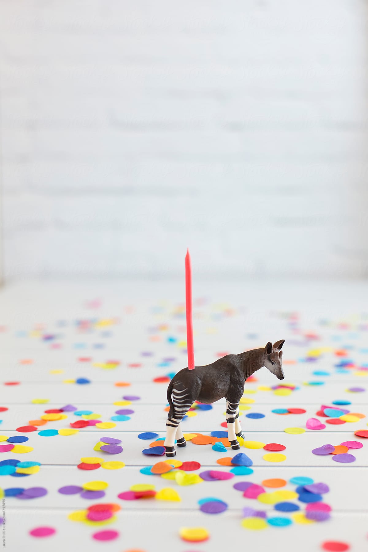 Okapi toy decorated with birthday candle standing amongst colorful confetti