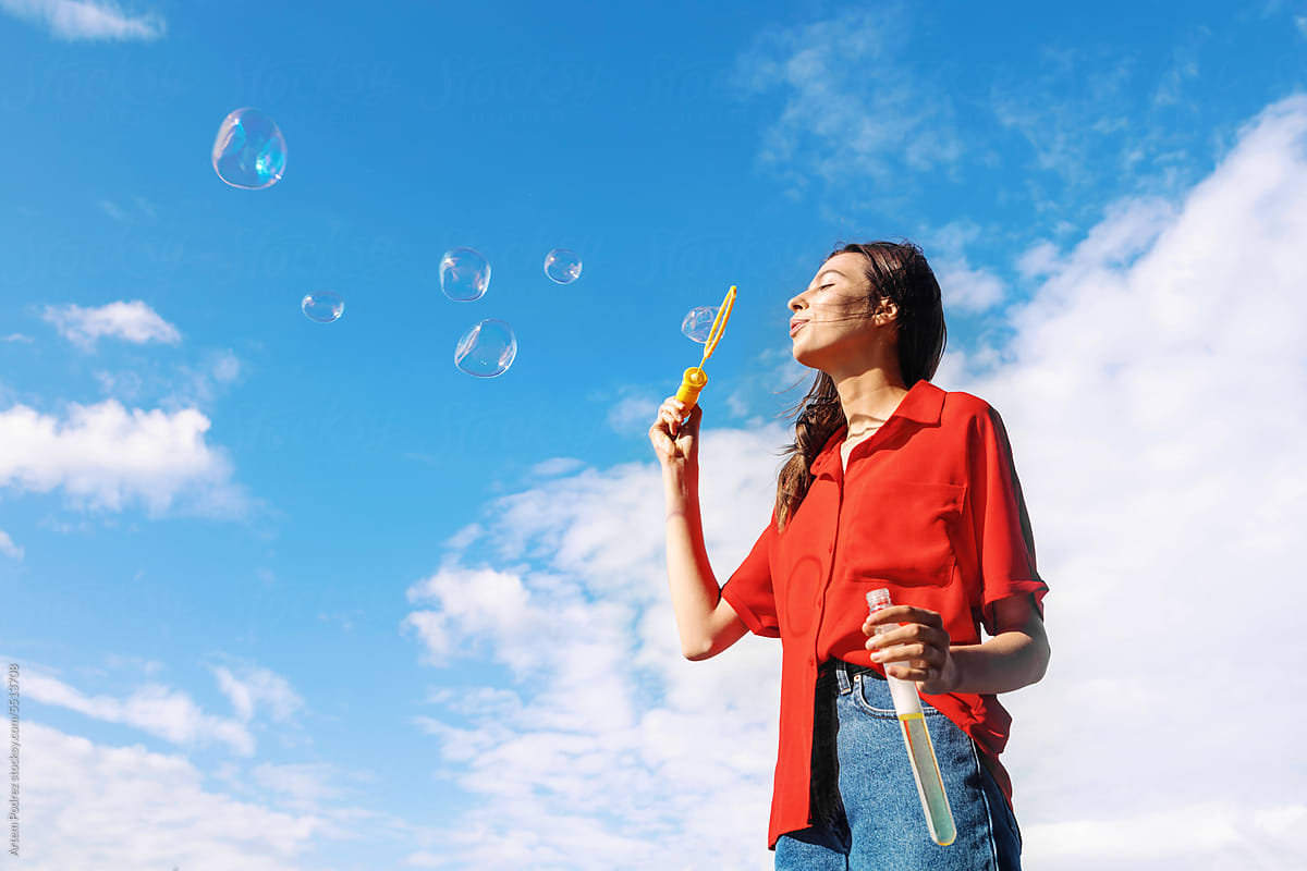 A young woman in a red shirt blows soap bubbles