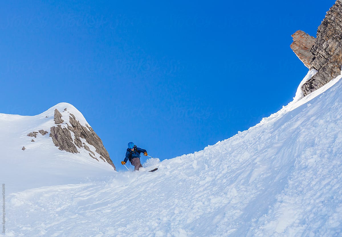 Male skier in blue clothing skiing a steep mountain snow slope in Austria.