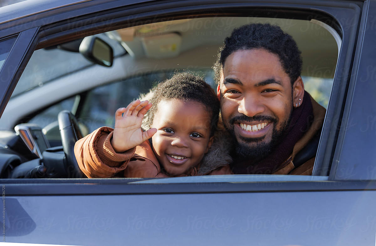 Cheerful boy waving while sitting with father in car