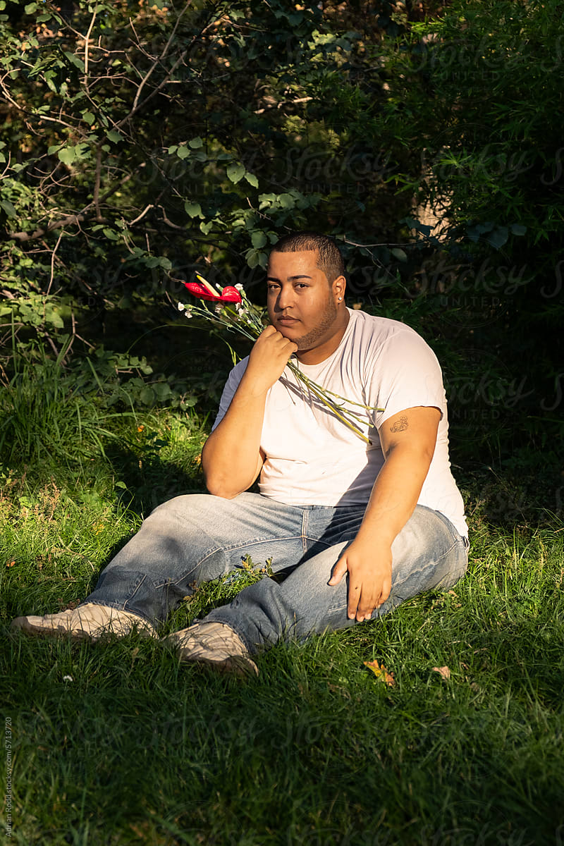 Black Plus-Size guy sitting on the grass looking into the camera.