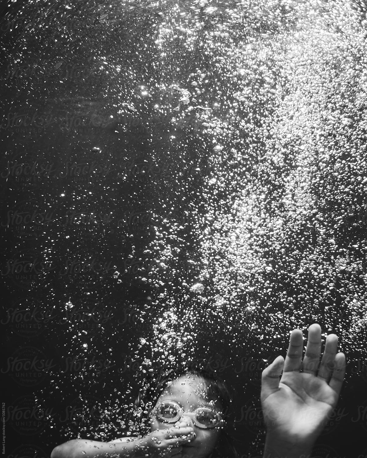 A child holds their nose and breath underwater surrounded by air bubbles