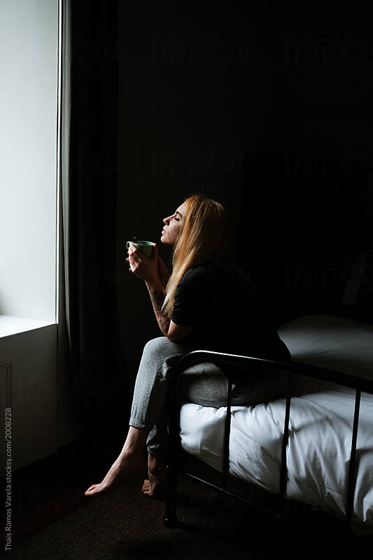 sleepy blonde woman sitting on the bed taking a cup of coffee in the morning