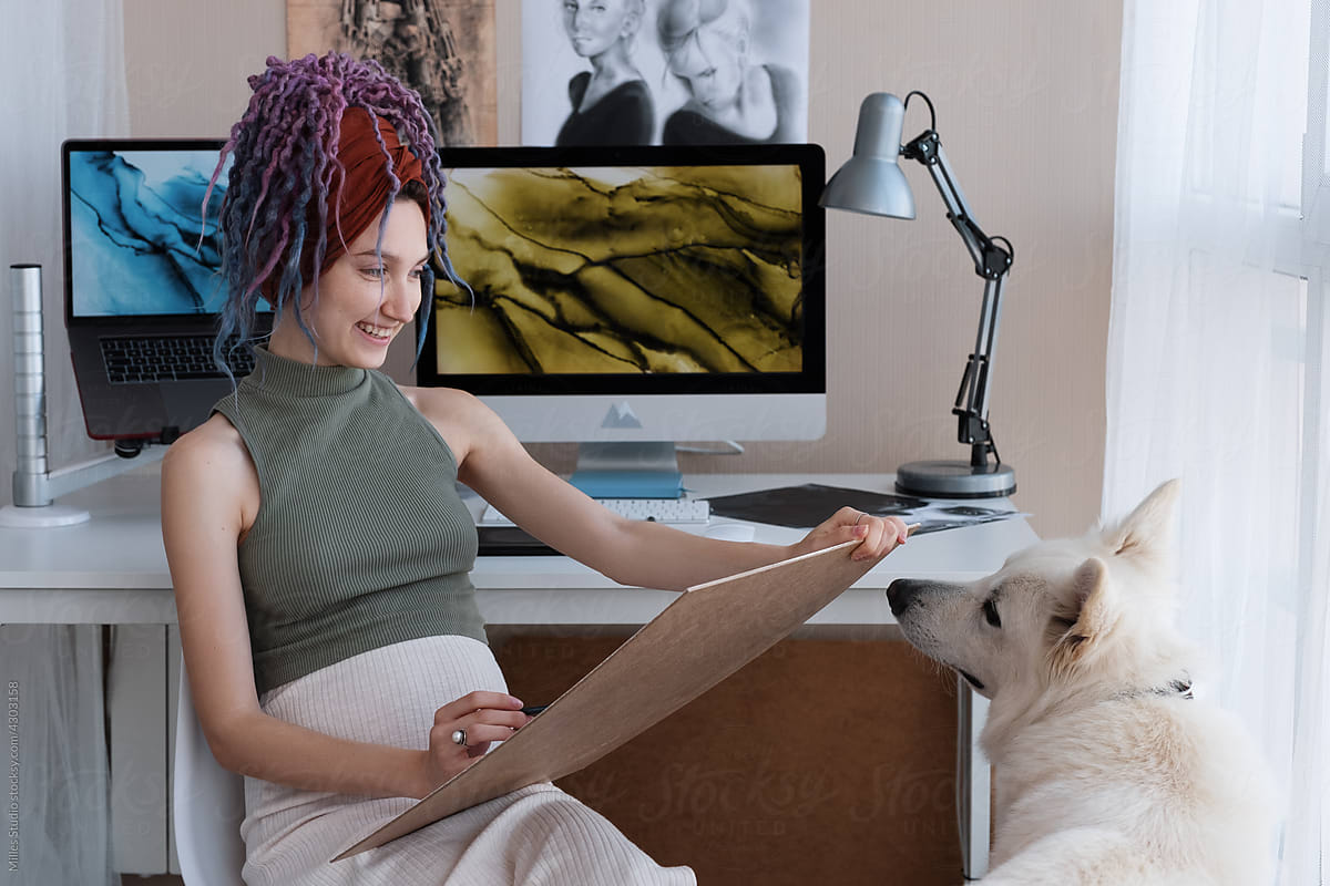 Merry female artist drawing picture near dog