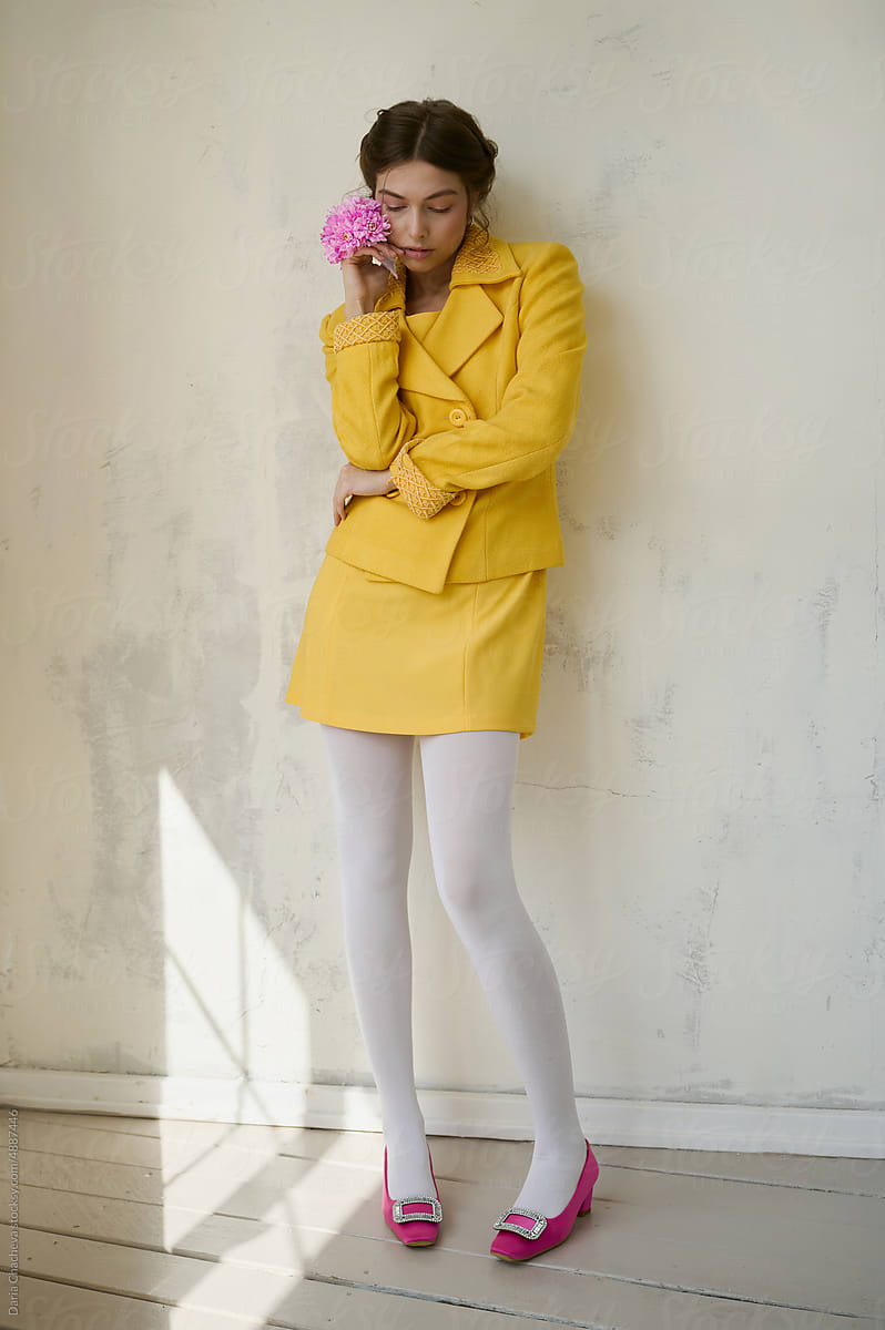 Young girl in a yellow suit with a pink flower near a white wall.