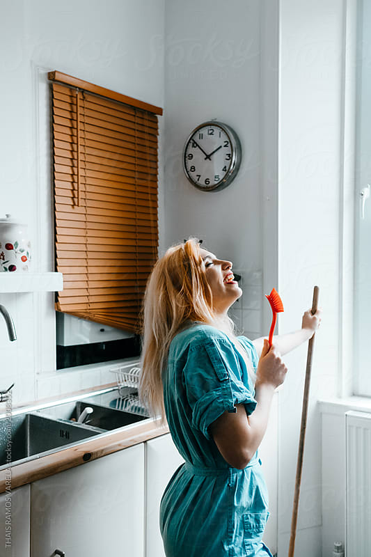 woman singing at the kitchen with a scrubber used like a microphone