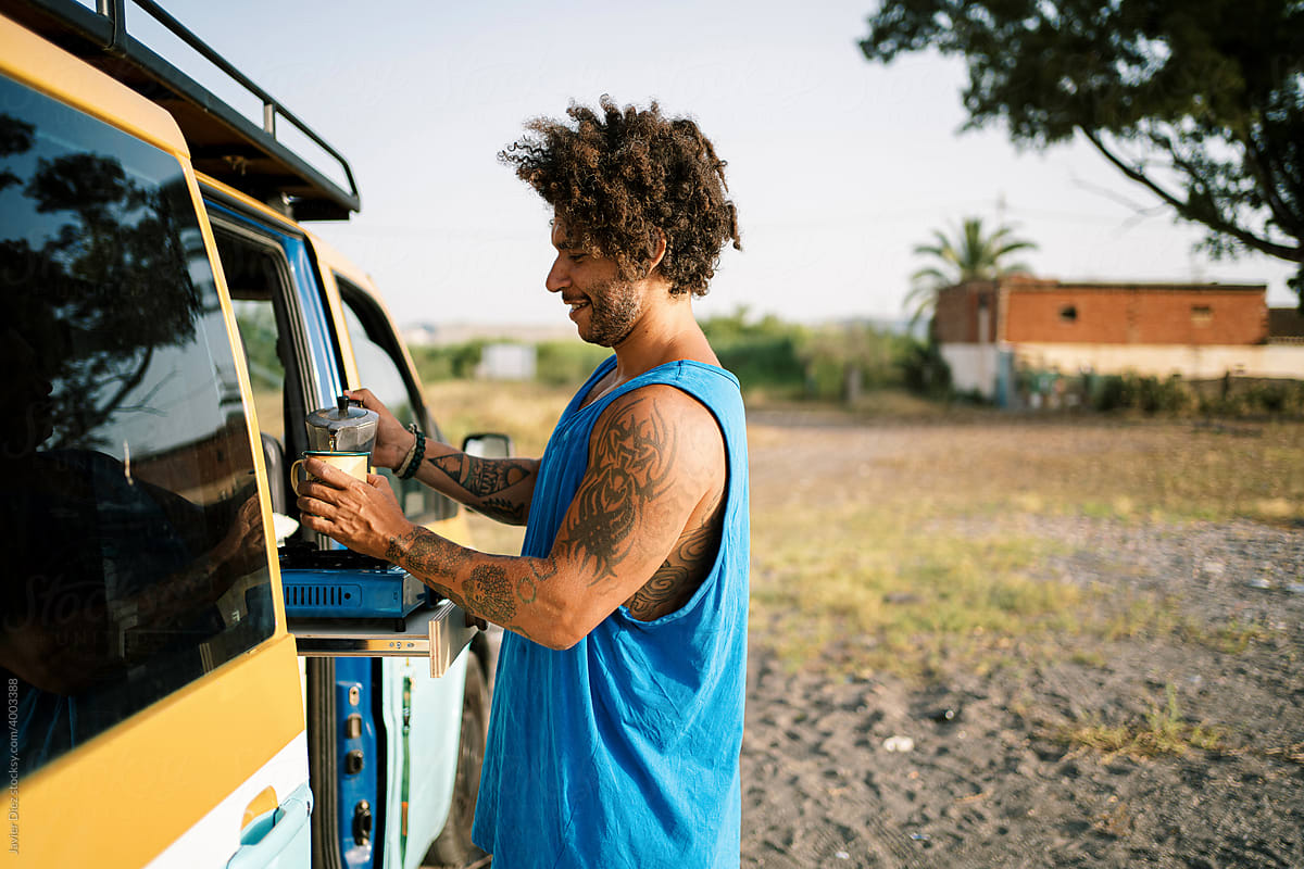 Hipster traveler relaxing near camper van with coffee in nature