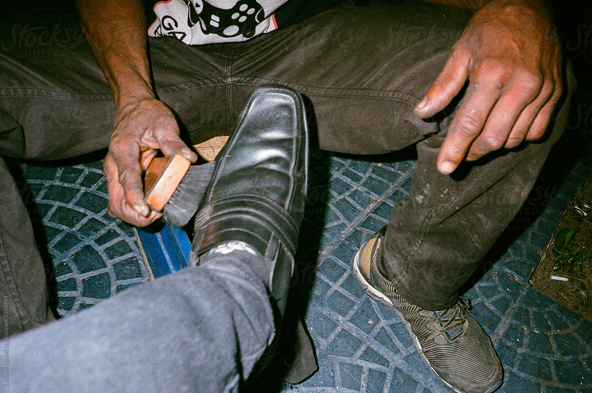 Shoe shiner street worker polishing his client\'s leather shoes