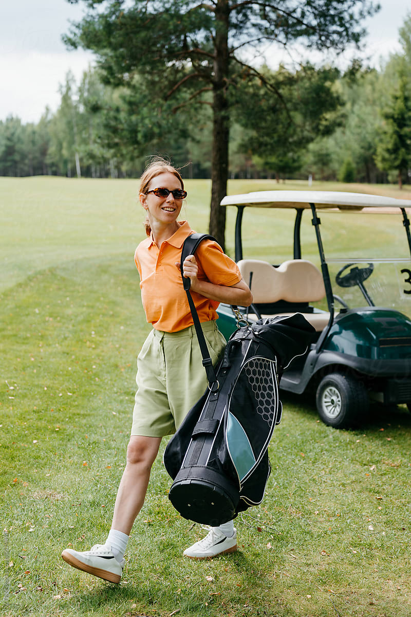 A woman carries a bag of golf equipment walking on a golf course