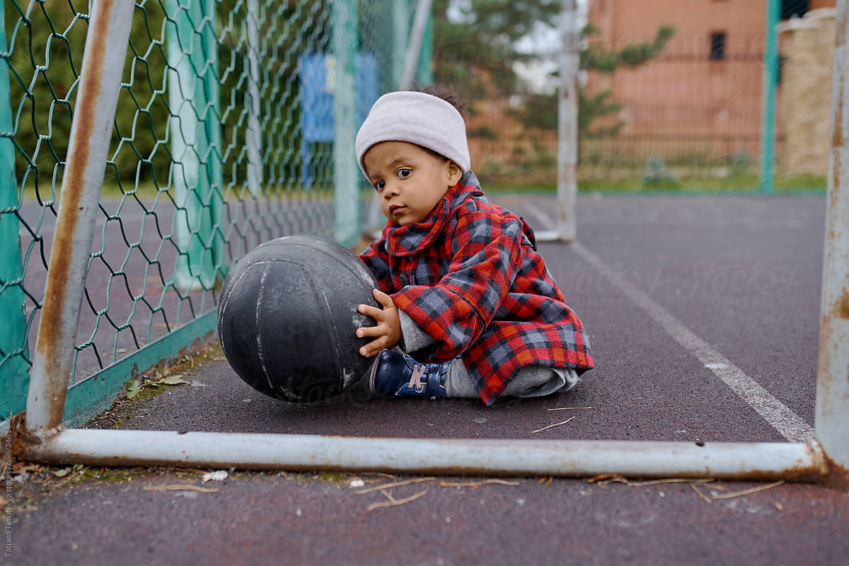 little girl in autumn clothes playing with a black basketball on the Playground